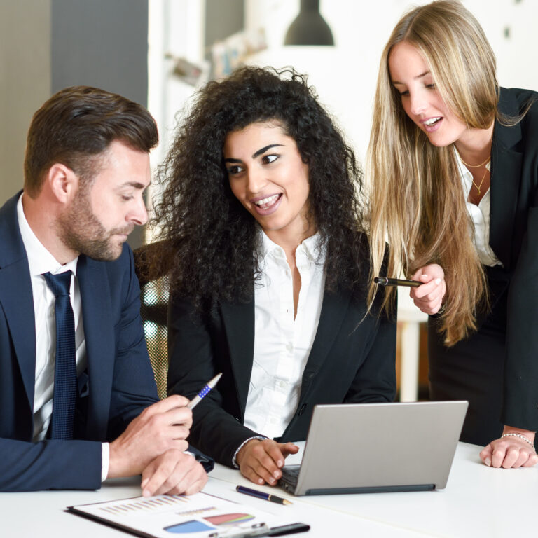 Multi-ethnic group of three businesspeople meeting in a modern office. Two women and a caucasian man wearing suit looking at a laptop computer.